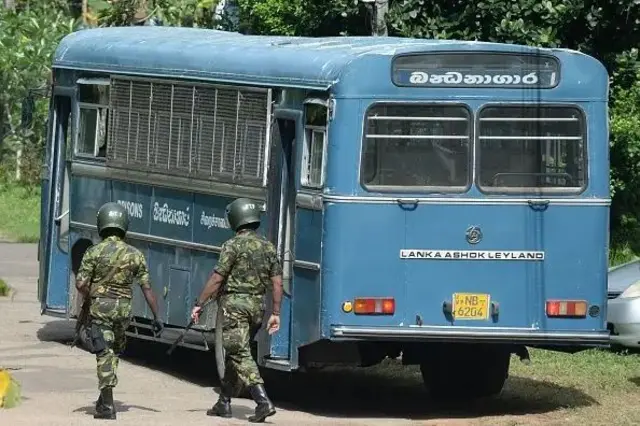 බන්ධනාගාර බස් රථයක් අසලින් ගමන් කරන පොලිස් විශේෂ කාර්ය බලකායේ නිලධාරීන් දෙදෙනෙක් 