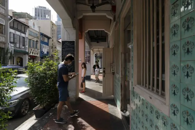 Para pejalan kaki yang mengenakan masker pelindung berjalan di sepanjang deretan rumah toko setinggi lima kaki di Ann Siang Hill, kawasan Tanjong Pagar, Singapura, pada Sabtu, 14 November 2020. Dengan atap genteng terakota, jendela kayu bergaya Prancis, dan fasad berwarna cerah, rumah toko khas Singapura menjadi aset properti terbaru yang diincar oleh kantor keluarga, taipan, dan investor real estat. 