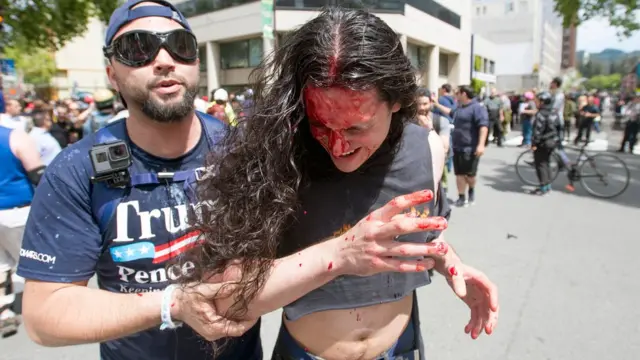 一名示威者扶着另一名血流披面的示威者。