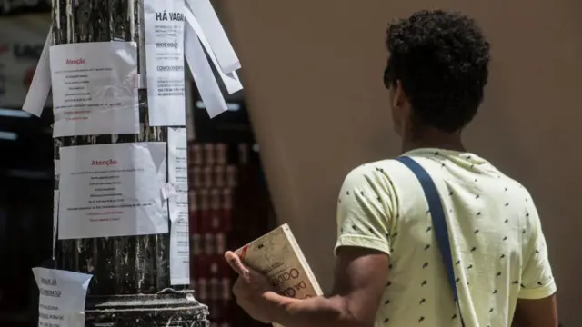 Un joven mira ofertas de trabajo colgadas en un poste