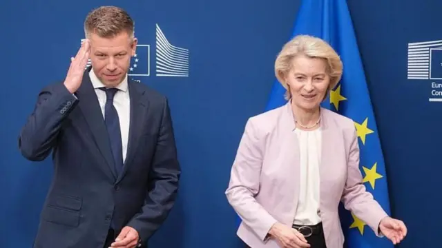 Magyar ve von der leyen yanyana AB bayrağı önünde. 