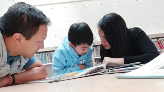 Niño leyendo con ayuda de sus padres