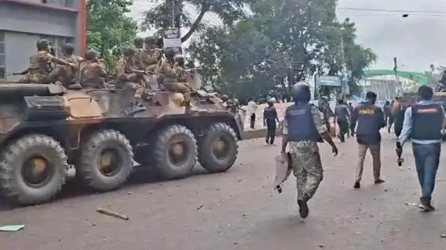 রাস্তা দিয়ে যাচ্ছে সেনাবাহিনীর ট্যাংক, ওপরে অস্ত্র হাতে বসে আছেন কয়েকজন সেনাসদস্য। পাশ দিয়ে যাচ্ছেন আইনশৃঙ্খলা বাহিনীর কয়েকজন সদস্য