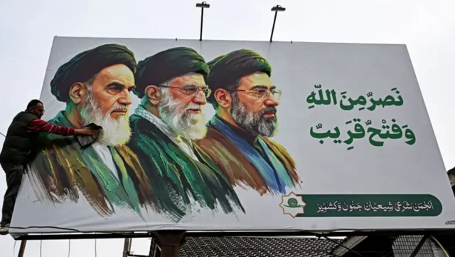 یک بیلبورد که تصویر سه رهبر جمهوری اسلامی بر آن دیده می‌شود، مردی در حال تمیز کردن بیلبورد است