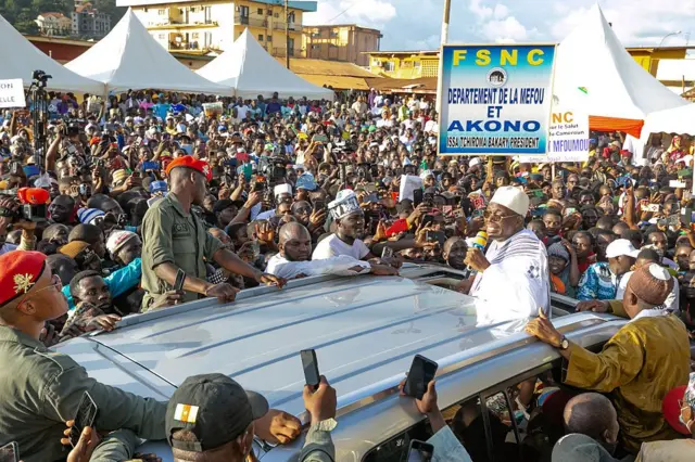 Issa Tchiroma Bakary debout dans un véhicule en train de parler à une foule qui l'entoure.