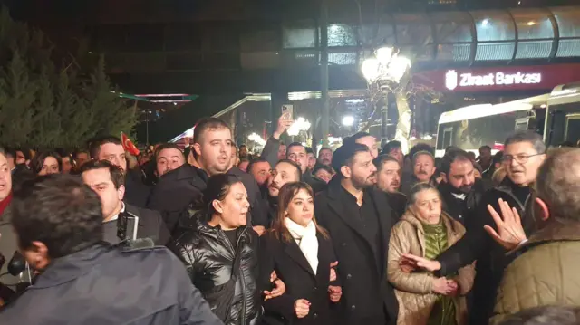Ortada gamaze taşcıer ve kolkola girmiş kalabalık protesto yürüyüşü yapmak istiyor. 