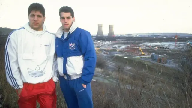 تونی میولا و جان هارکز (سمت راست) با پس‌زمینه‌ای از برج‌های تینزلی در شفیلد. آنها پس از حضور در جام جهانی ۱۹۹۰ ایتالیا به تیم شفیلد ونزدی پیوستند و هارکز سه فصل برای این تیم بازی کرد