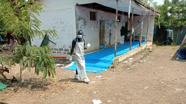 ጭንብር የለበሰ የጤና ባለሙያ ጤና ጣቢያ ውስጥ እየተንቀሳቀሰ