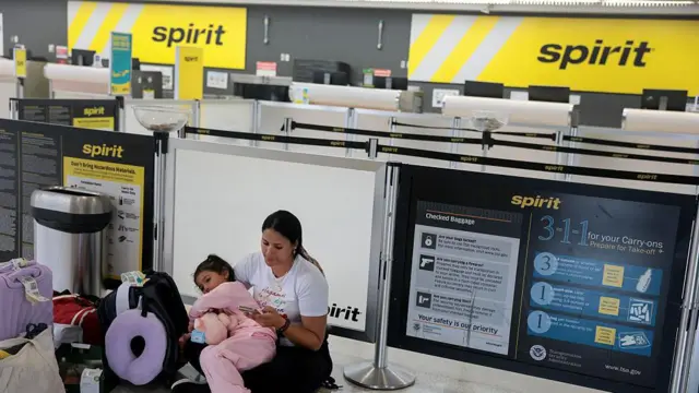 Una mujer colombiana con su hija de brazos, sentada en el counter vacío de Spirit Airlines