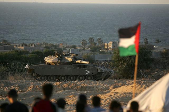 فتيان فلسطينيون ينظرون إلى دبابة إسرائيلية في جنوب قطاع غزة