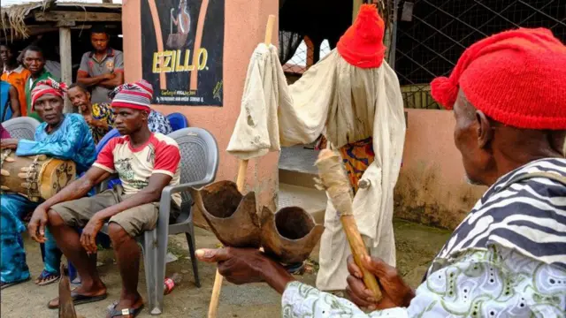 Ndị mmadụ na-eme omenala nọ ọdụ n'oche dịka nwoke ji osisi nakwa akụrụngwa ogene na-aka