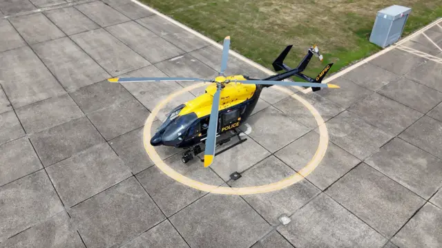 一架警用直升机停在艾塞克斯(Essex)的一处停机坪上,俯瞰画面中可见混凝土地面上绘有一个大型黄色降落圆圈,正位于直升机下方。