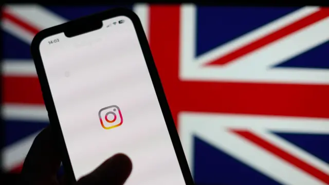 Um smartphone exibe a tela inicial do Instagram, com seu logotipo destacado sobre um fundo branco, enquanto ao fundo aparece desfocada a bandeira do Reino Unido.