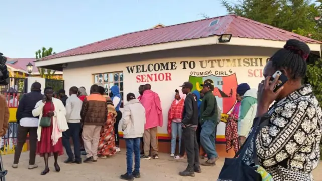 Ọpọlọpọ awọn obi lọkunrin ati lobinrin duro si ẹnu ọna abawọle sile ẹkọ ti ijamba ina ti waye