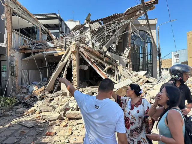 Personas en una calle de Pereira miran con asombro los daños que dejó el terremoto en diferentes propiedades.