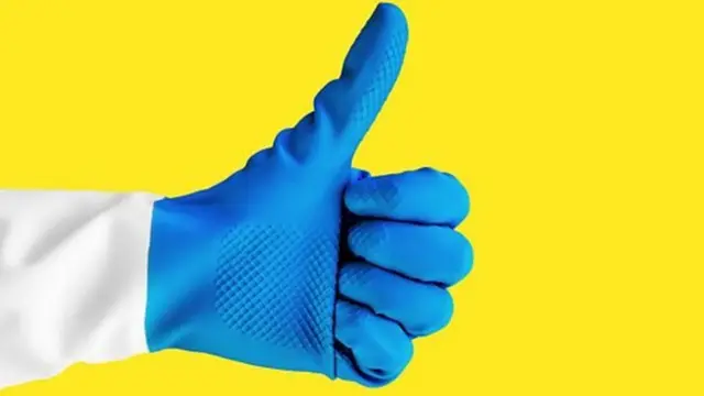 Main gantée d'un nettoyeur qui lève le pouce sur fond jaune
