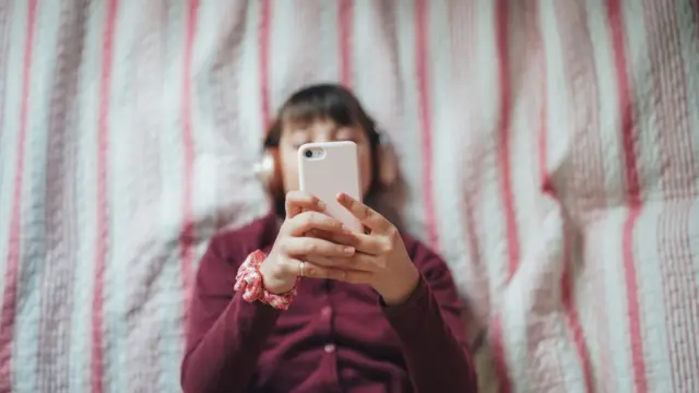 Foto vista do alto, com uma adolescente segurando um celularroleta do facebookfrente ao rosto 