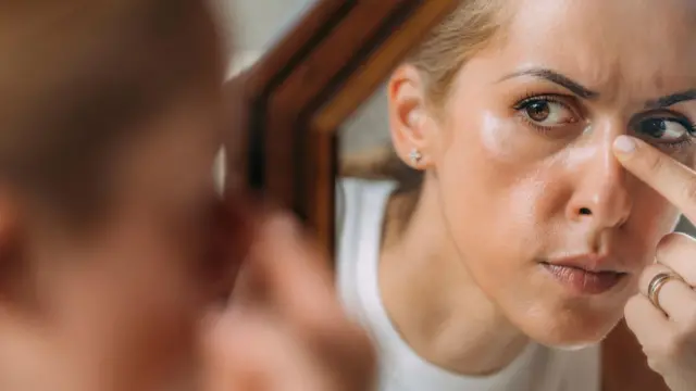 Жінка розглядає у дзеркалі свій ніс 