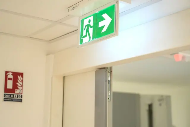 A green and white safety sign indicating the direction of an evacuation towards the emergency exit in case of fire or disaster 