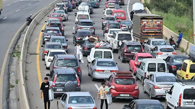 Carros parados em congestionamento em uma estrada, com pessoas vendendo produtos para os motoristas