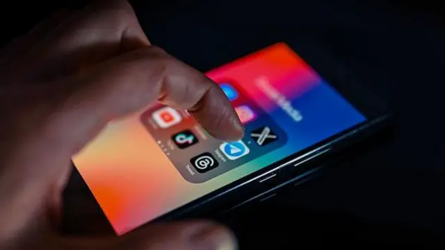 Колаж, на якому зображений екран смартфона з кольоровими іконками соціальних мереж, до яких торкається рука. 