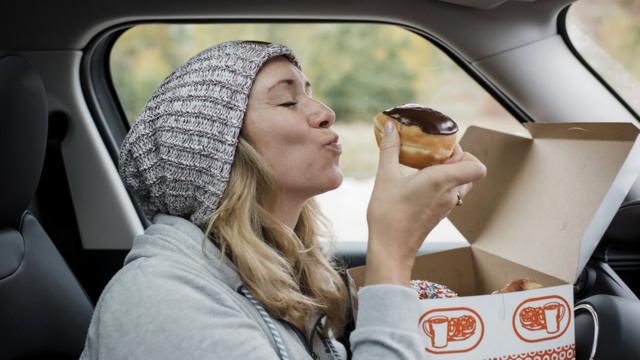 Женщина ест пончик в автомобиле