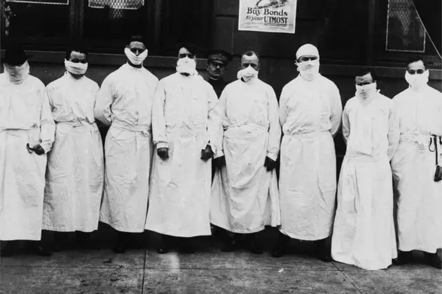 Doctors, army officers, and reporters wear surgical gowns and masks while making a tour of a hospital to observe Spanish influenza treatment of patients. -