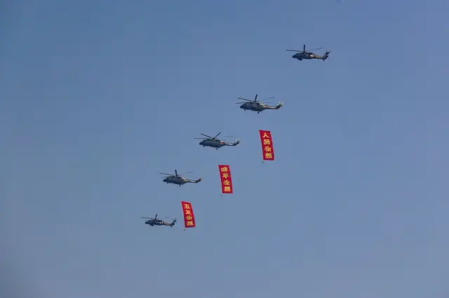 直升机在北京天安门广场上空飞过，挂着的旗帜分别写着“人民必胜”、“和平必胜”、“正义必胜”。