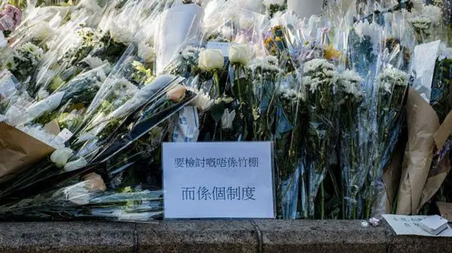 2025年11月29日,巿民在宏福苑附近公园摆放鲜花悼念罹难者,一张纸张上写着:“要检讨的不是竹棚,而是制度”。