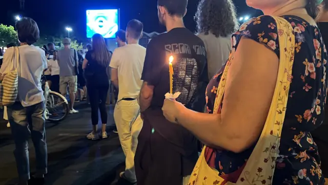 Жена која држи свећу у руци стоји заједно са другим демонстрантима