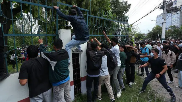 A group of ten men stood at a wall as one makes his ascent over the railings outside the parliament building in Kathmandu