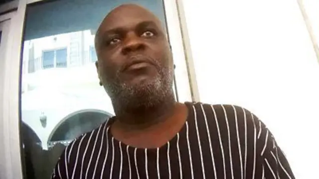 Imagem filmada secretamente de Charles Mwesigwa, vestindo uma camisa listrada preta e branca