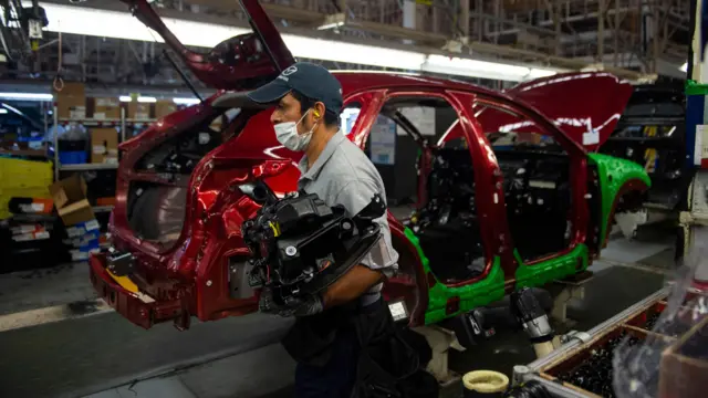 A worker carries a component in a car assembly plant in Mexico 