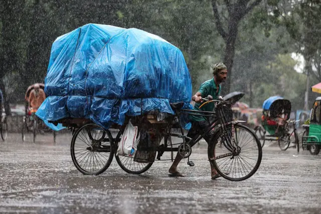 বৃষ্টির মধ্যে মালামাল পরিবহন করছেন ভ্যানচালক