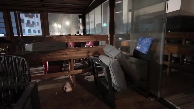 El interior oscuro de un bar muestra mesas y asientos tirados