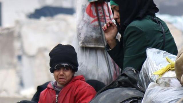 Niño llorando y una mujer esperan ser evacuados de Alepo