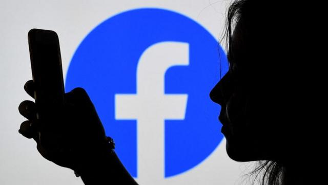 Sombrasite bra betmulher olhando para celular, com logo do Facebook no fundo