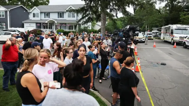 一群民眾聚集在市郊街道上,站在警方封鎖線與警車後方