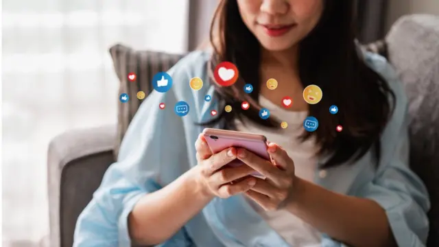 Young woman looking at her smartphone with emoji graphics added in the background