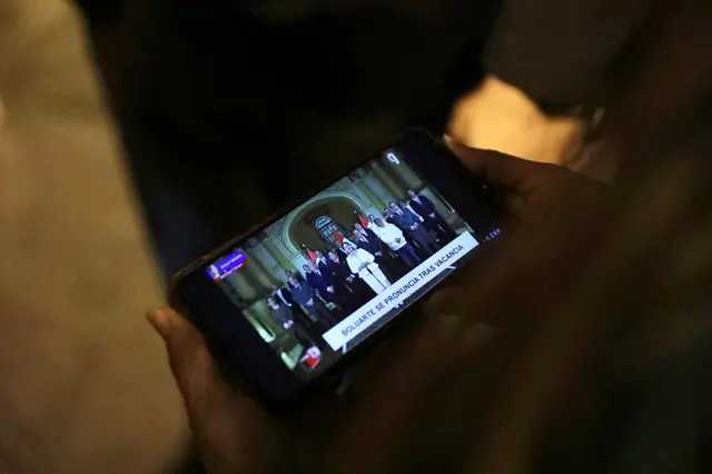 Una persona sostiene un teléfono mientras se transmitía el último discurso de Dina Boluarte desde el palacio presidencial.