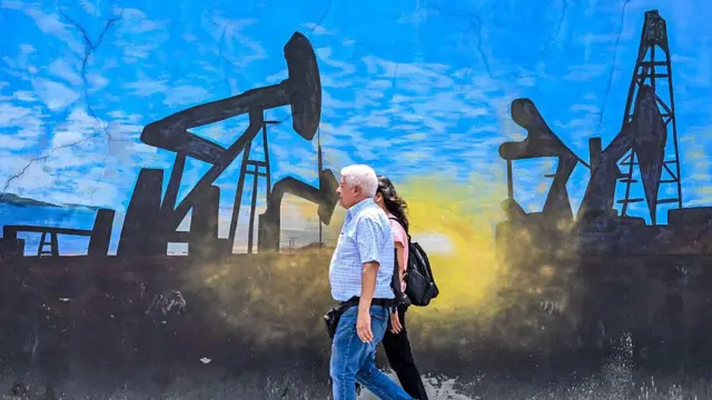 Pessoas caminham em frente a um mural que representa bombas de petróleo em Caracas
