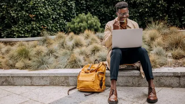 Homem sentado no meio fio, comendo e sorrindoesporte bet aviatordireção a laptop