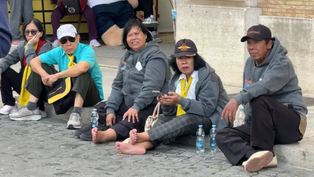 Туристи сидять на землі на площі Святого Петра 