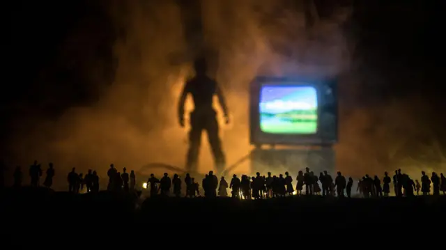 مفهوم الأخبار الكاذبة على التلفاز. صور ظلية لحشد ينظر إلى صندوق تلفزيوني عملاق. ديكور فني إبداعي. تركيز انتقائي
