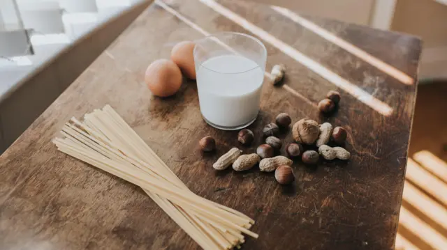 Grupa powszechnie znanych alergenów na stole, w tym jajka, mleko, orzechy i makaron.