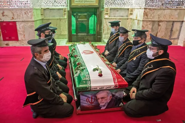 Soldiers wearing face masks kneel around a decorated coffin