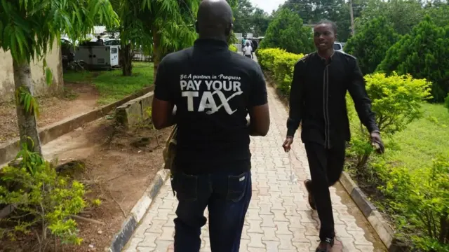 Man wey wear Tshirt wey dem write "Pay your tax".