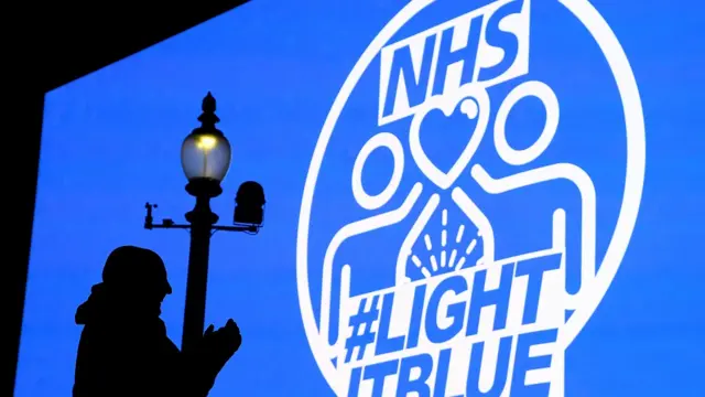 A person is seen in silhouette, applauding the work of the NHS, in front of big screen in Piccadilly Circus