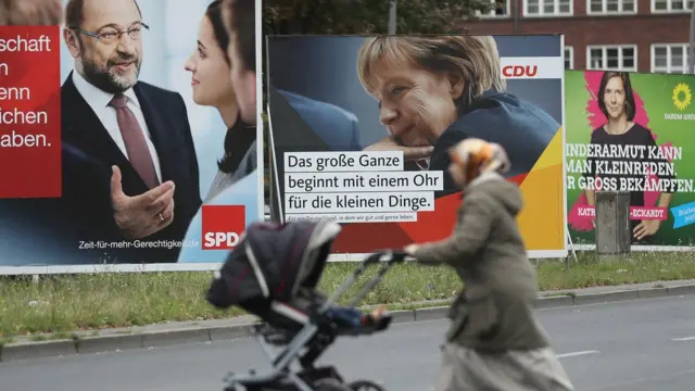 Seçim reklamlarının önünde bebek arabasıyla yürüyen başörtülü bir kadın