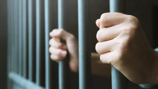Pessoa segurando barras de cela de prisão